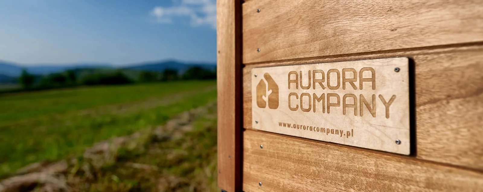 Aurora-Company-Schild auf einer Holzfassade mit Blick ins Grüne