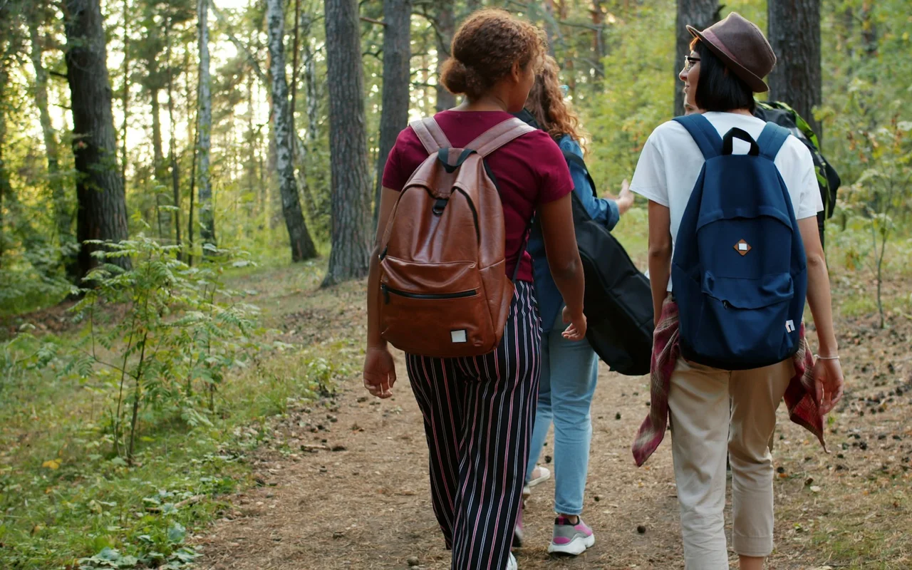 Freunde mit Rucksäcken unterwegs auf einem Waldweg.