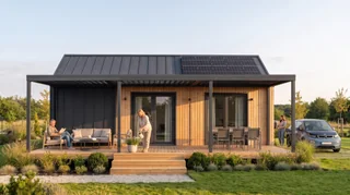Menschen lesen und pflegen Pflanzen unter der Aluminiumterrasse vor Evergreen mit PV, daneben ein Elektroauto an der Wallbox