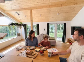 Zwei Erwachsene und ein Kind frühstücken gemeinsam am Holztisch im lichtdurchfluteten Evergreen