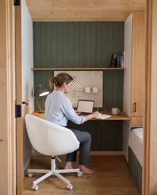 Frau arbeitet am Laptop an einem eingebauten Holzschreibtisch im Evergreen mit grüner Rückwand
